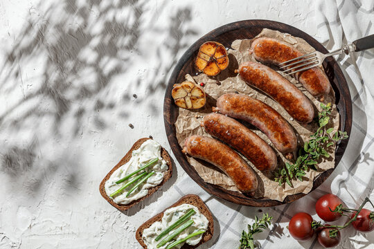 Grilled beef meat sousage on white wooden plate with herbs and fresh vegetables. Sunny day, barbeque. Indgridients on a table, top view