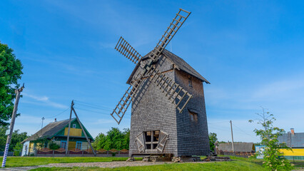 Fototapeta na wymiar Vintage wooden windmill with cycling track on blue sky background. Historical farm house windmill.