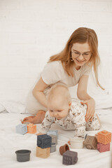 Portrait of young smiling mother mom lying with little cute plump infant baby playing with modern pastel silicone bowls.