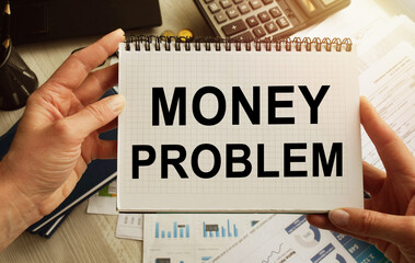 A business woman at a table in the office holds a notebook in her hands with the inscription MONEY PROBLEM. Desktop with documents. Lettering is important for promoting your company.