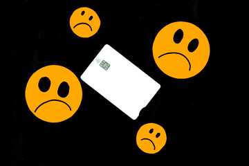 illustration of orange paper emoticon faces cut out with sad gesture and a white bank card on black...