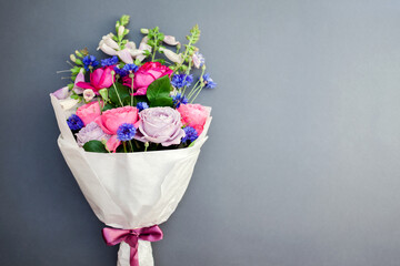 Fresh bouquet of roses foxgloves bachelor buttons flowers wrapped in paper and arranged on background.