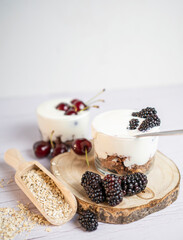 Yogurt with blackberries and cherries, fresh fruit with oat biscuit, white wood background.