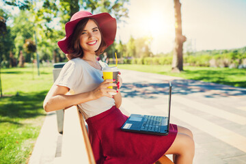 Fototapeta premium Girl with a laptop on a bench in the park in summer