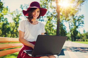 Girl with a laptop on a bench in the park in summer