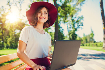 Girl with a laptop on a bench in the park in summer