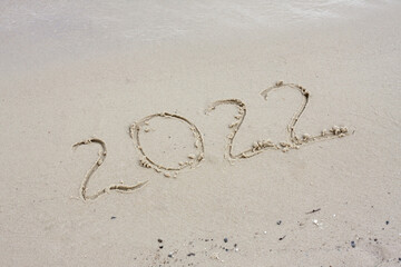 Date 2022 handwritten in sand. Happy New Year greeting card.