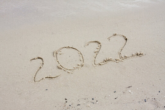 Date 2022 handwritten in sand. Happy New Year greeting card.