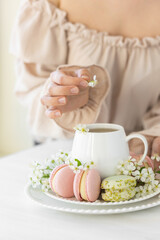 Traditional delicious French dessert - sweet homemade macarons on a vintage plate. Colourful tasty macaroons served on a white china with herbal tea. Decorated with fragile cherry tree flowers.