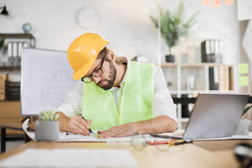 Architect man or male builder hold pen and ruler, writing and drawing architectural project, work on laptop computer on the desk at workplace.