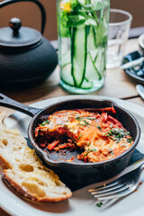 Half eaten freshly made shakshuka with spiced tomato, red pepper, feta, egg, coriander and pieces of homemade sourdough, served in iron pan, healthy vegetarian breakfast