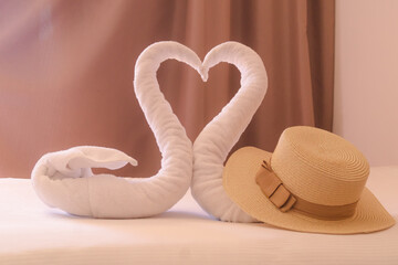 A beach hat with a seashell lies on the bed. Towels in the shape of swans in the background. Summer...