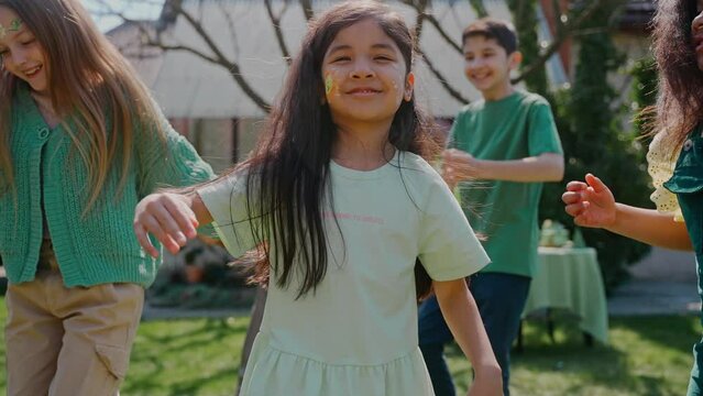 Girl looking at the camera dancing at the birthday party at the backyard. Green-themed birthday party. Boys and girls dancing and spinning outside on a sunny day. High quality 4k footage