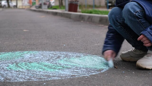 a girl of 6 years old draws the planet earth on the pavement with chalk, a child in a jacket and hat plays outdoor