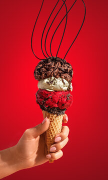 Holding in hand cone with ice cream sorbet gelatto balls with taste of chocolate, strawberry and vanilla ,isolated on red background. Concept with motion .hard light