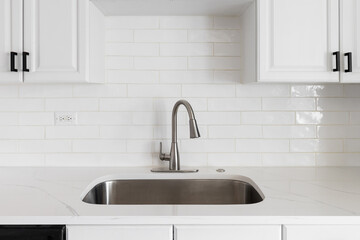 Kitchen sink detail shot with a subway tile backsplash, granite countertop, white cabinets, and a...