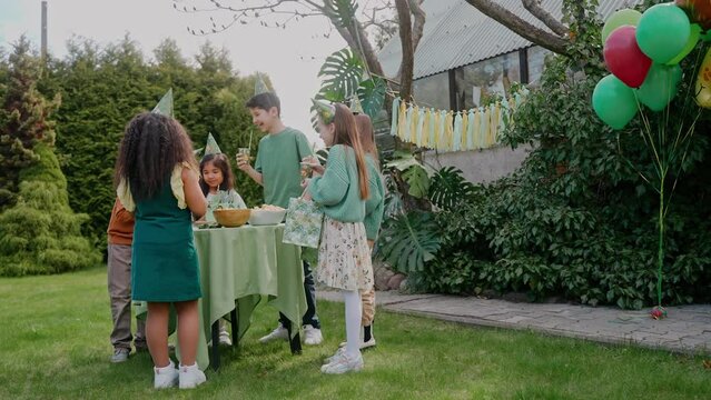 Kids having a green-themed birthday party at the backyard, eating at the table. Green-themed birthday party. Children celebration meal outside of the house. High quality 4k footage