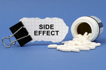 On the blue surface lies a jar of pills and a clip with paper on which is written - SIDE EFFECT