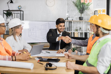 Multiethnic architects, designers and engineers sitting at table and greeting each other with hands...