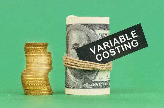 On a green surface are coins and dollars in a bundle. On the dollar sign with the inscription - Variable Costing