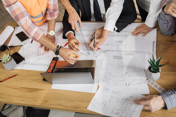 Close up of architects, engineers and designers sitting together at table and analysing blueprints. People of different ages and races working at office. Creation of construction project.