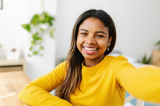 Happy young hispanic latina teenager girl taking selfie portrait with mobile phone app on bedroom