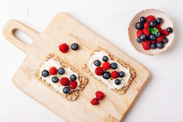 Sandwiches with blueberries and raspberries on cutting board on white wooden table. Healthy breakfast. Top view, flat lay