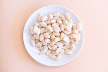 Uncooked Gnocchi lays on a white plate on a yellow background. Fresh. Ingredient. Background. Uncooked. Cuisine. Traditional. Cookery. Dumpling. Dough. Gourmet. Italy. Homemade. White. Healthy
