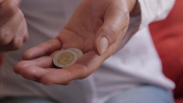 Manos de persona contando monedas mexicanas