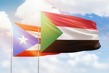 Sunny blue sky and flags of sudan and puerto rico