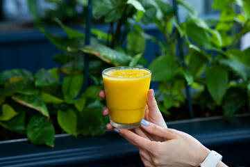 Woman hand holding glass jar of orange smoothie, fresh juice against blue background. Healthy beverage, vegan, vegetarian concept. Banner with copy space