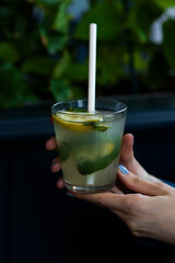 Mojito cocktail or mocktail with lime, mint, and ice in glass on blue background. Summer cold alcoholic non-alcoholic drink, beverage and cocktail. hold in hands