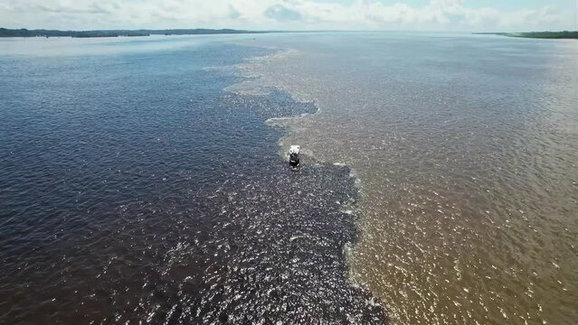 Boat sailing at Meeting of the Waters tourism landmark at Manaus Amazonas Brazil. Brown Amazon river side Black Negro River with two different colors. Amazon rainforest Brazil. Manaus Amazonas Brazil.