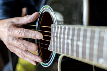 Elderly man right hand with amputated middle finger playing a black acoustic guitar