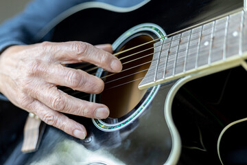 Elderly man right hand with amputated middle finger playing a black acoustic guitar
