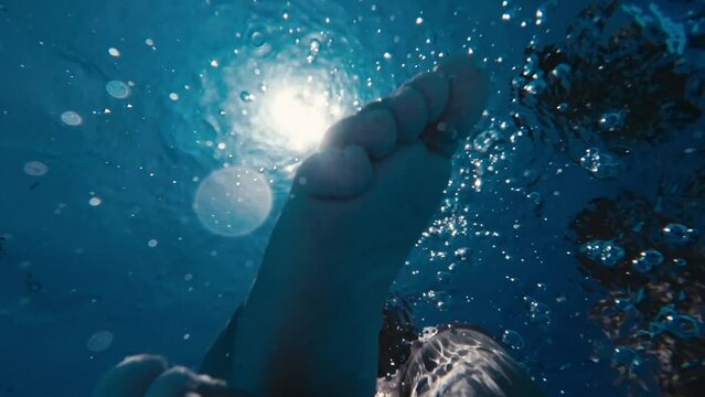 Child bare feet above blue water in swimming pool.