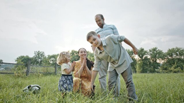 Family spending time near planted tree sapling. Ground level of siblings giving high five to each other then little daughter clapping hands with mother and kissing father after planting tree sapling
