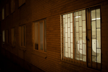 Window in building in evening. Grille on window at night.