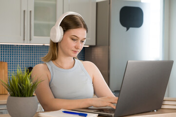 Young female student in headphones for listening and wrtiting down the lecture.