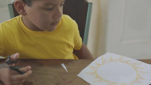 Latin boy in yellow sweater painting on the table in the house
