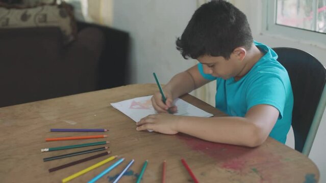 Latin boy with blue sweater painting with colored pencils on white sheet