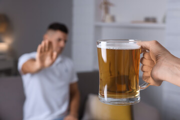 Man refusing to drink beer in kitchen, closeup. Alcohol addiction treatment