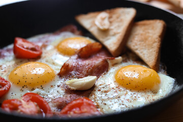 Delicious fried eggs with bacon and tomatoes in pan, closeup