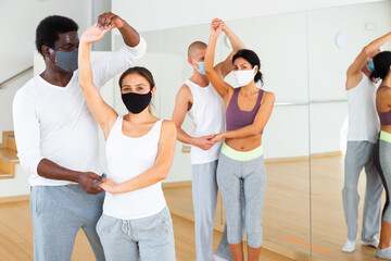 Multiethnic group of adult people wearing protective masks practicing ballroom dances in pairs in...