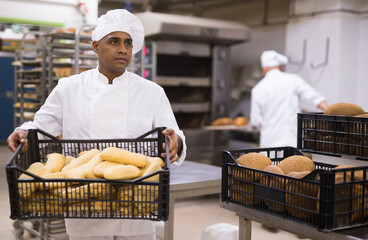 man in chefs uniform with bread in tray in bakery