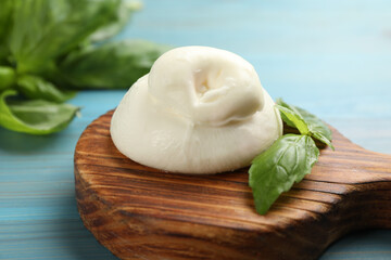 Delicious burrata cheese with basil on light blue wooden table, closeup