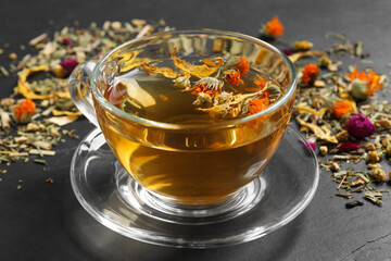 Freshly brewed tea and dried herbs on black table, closeup