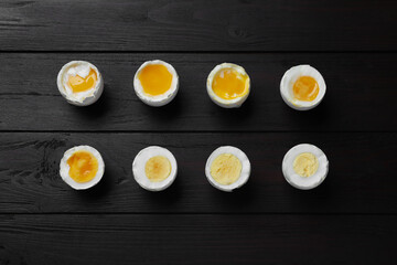 Different readiness stages of boiled chicken eggs on black wooden table, flat lay