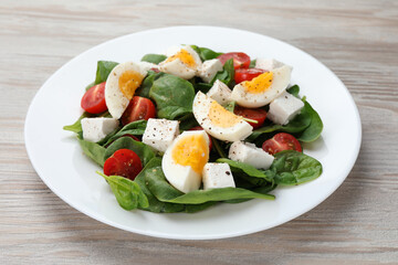 Delicious salad with boiled eggs, feta cheese and tomatoes on wooden table, closeup