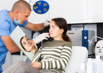 Male beautician in gloves examining face skin of young woman before procedure at cosmetology clinic